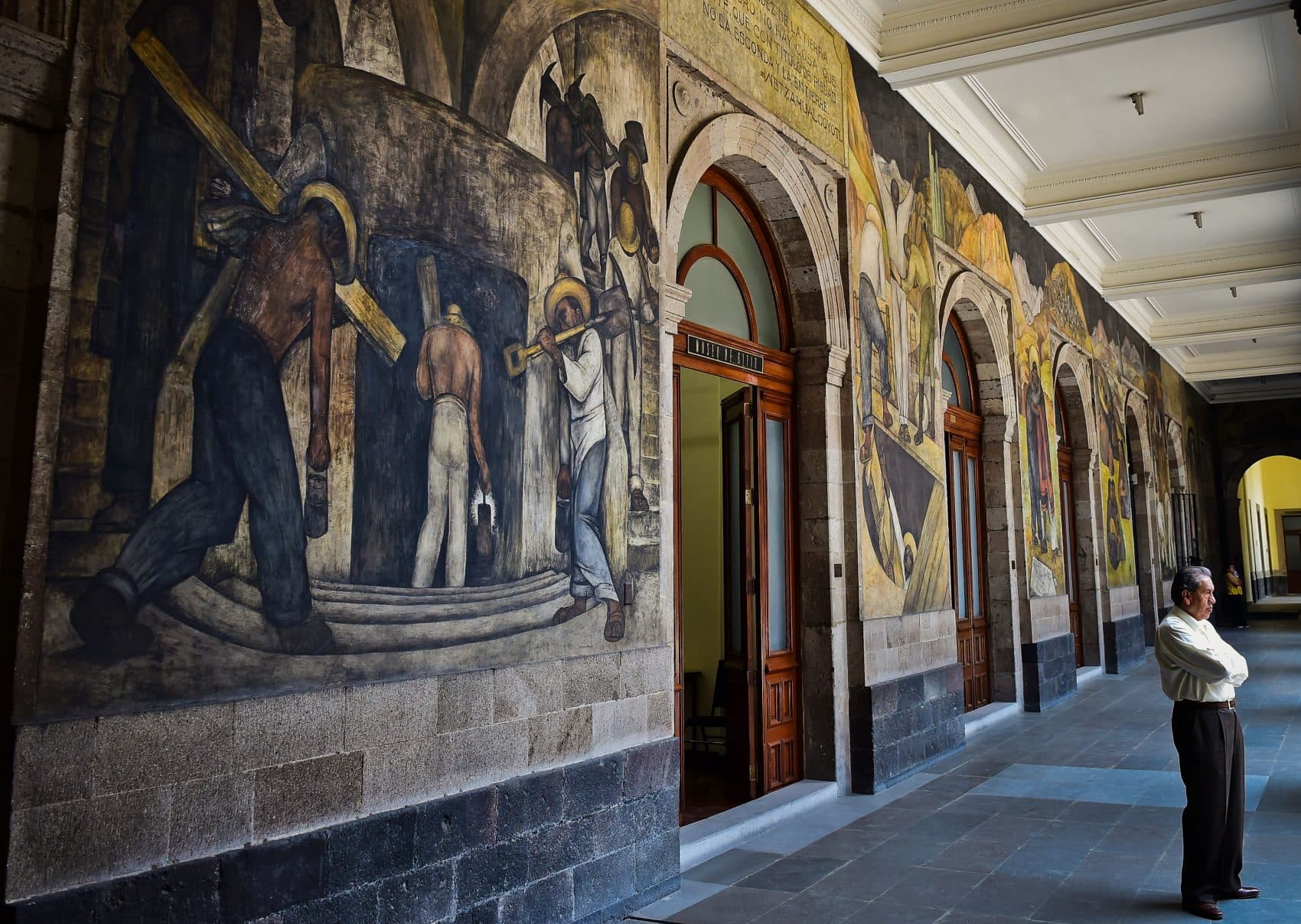 A man stands next to murals by Mexican artist Diego Rivera in the Education Secretariat in Mexico City on April, 6, 2017. Rivera was the most visible figure in Mexican muralism, a large-scale public art initiative that emerged in the 1920s in the wake of the Mexican Revolution. (Ronaldo Schemidt/AFP/Getty Images)