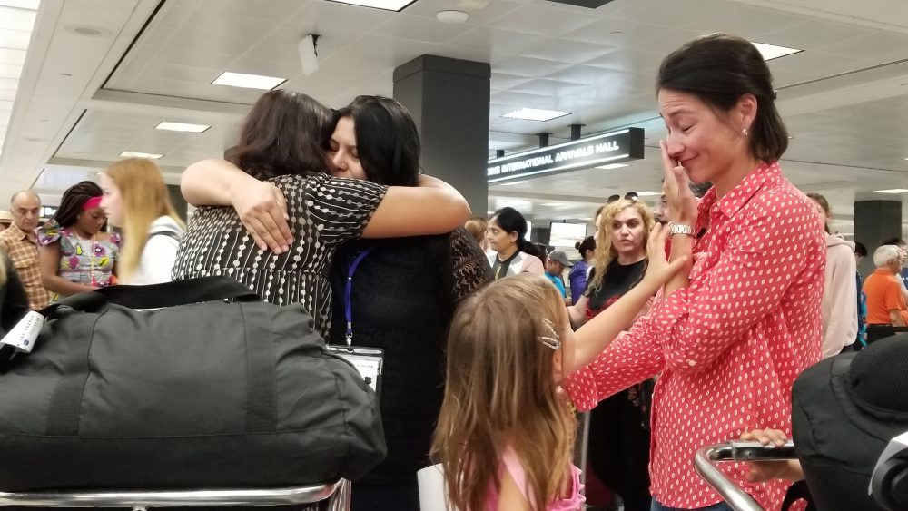 Sisters Rahila, left, and Shaista Sadiq, right, embrace at Dulles Airport as family friend Kristin Kim Bart looks on. The sisters went through a two year vetting process before being admitted as refugees to the U.S. Now, they’re among the last refugees to be resettled in the before new refugee admissions guidelines go into effect next week. (Carmel Delshad/WAMU)
