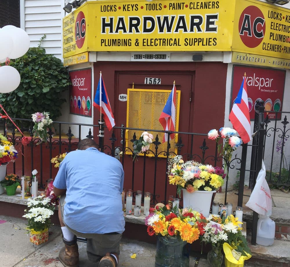 A man tends to a growing memorial Wednesday for Andres Cruz, who was fatally shot during an apparent robbery of his AC Hardware store in Boston's Mission Hill. (Anthony Brooks/WBUR)