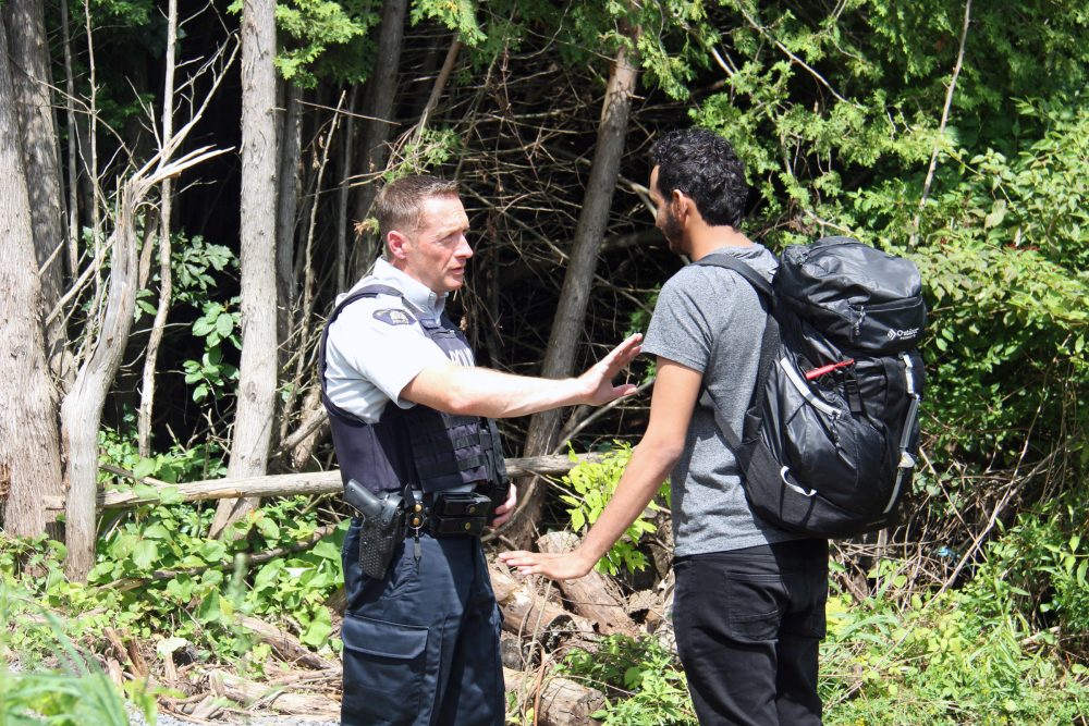 A Canadian police officer warns a young man from Yemen that if he illegally crosses into Canada in between checkpoints he will be arrested. If he proves to not be a threat to the public, the officers will help him fill out the asylum request paperwork. (Kathleen Masterson/VPR) 