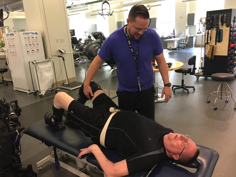 Physical therapist Dillon Bomer works with veteran William Geralds in the gym at the Polytrauma Rehabilitation Center in San Antonio. (Wendy Rigby/Texas Public Radio)