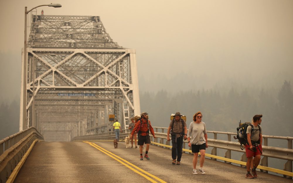 Pedestrians walk off the Bridge of the Gods, which spans the Columbia River between Washington and Oregon states, as smoke from the Eagle Creek wildfire obscures the Oregon hills in the background near Stevenson, Wash., Wednesday, Sept. 6, 2017. (Randy L. Rasmussen/AP)