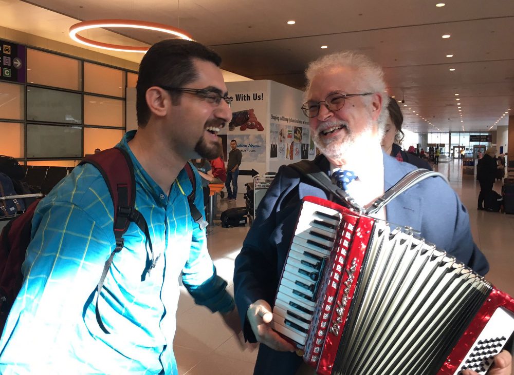Dr. Seyed Saravi, left, is welcomed to Boston Wednesday by Dr. Thomas Michel and Michel's accordion. (Shannon Dooling/WBUR)