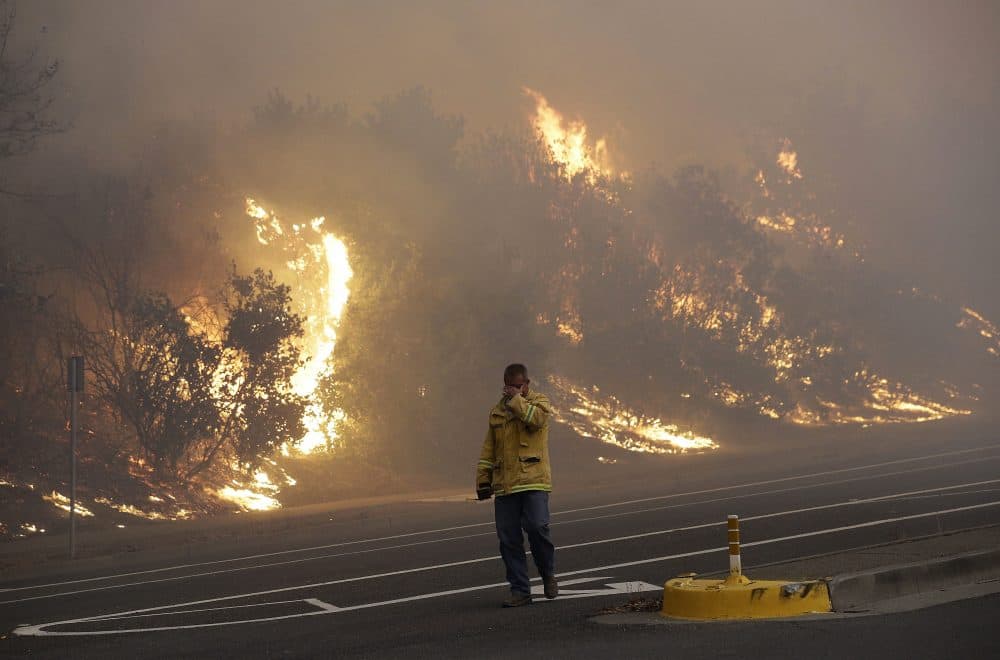 A firefighter covers his eyes as he walks past a burning hillside in Santa Rosa, Calif., Monday, Oct. 9, 2017. Wildfires whipped by powerful winds swept through Northern California, sending residents on a headlong flight to safety through smoke and flames as homes burned. (Jeff Chiu/AP)