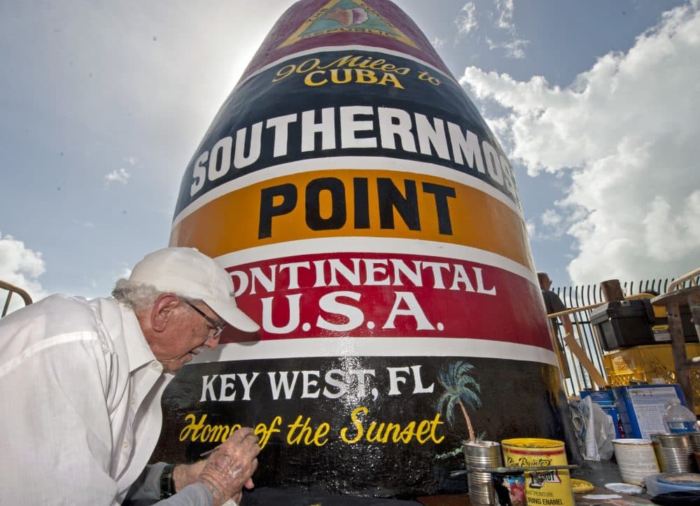 In this photo provided by the Florida Keys News Bureau, artist Danny Acosta completes lettering the Southernmost Point in the Continental U.S.A. marker Monday, Oct. 23, 2017, in Key West, Fla. One of the most-photographed tourism icons in the Florida Keys was pummeled by Hurricane Irma on Sept. 10, stripping most of the paint and a large chunk of stucco. (Rob O'Neal/Florida Keys News Bureau via AP)