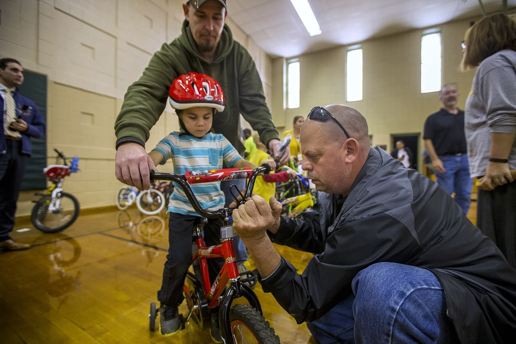 Five-year-old Christopher watches as Bob Charland, right, adjusts the handlebars of the bicycle he just received through the Pedal Thru Youth program at the Stefanik School in Chicopee. (Jesse Costa/WBUR)