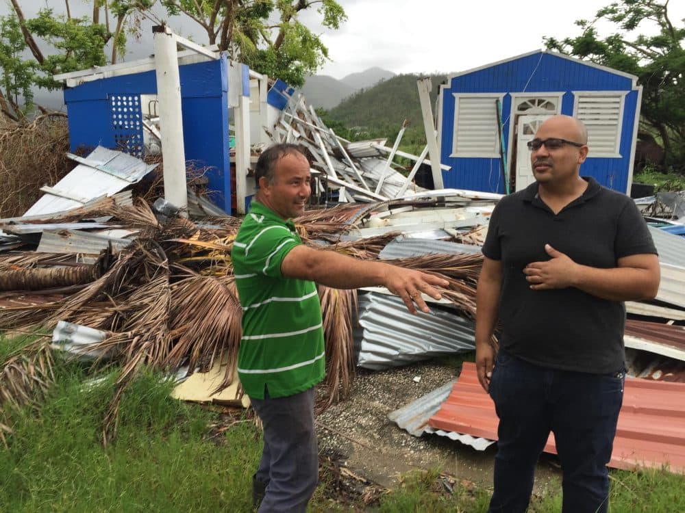 Jan Carlo Perez (right) talks with a neighbor this month in front of a house demolished in Patillas, Puerto Rico, by Hurricane Maria in September. (Tim Padgett/WLRN)