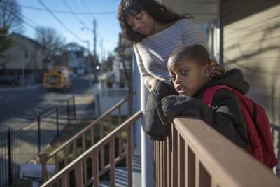 On the front porch, a 5-year-old student from Dorchester watches for his school bus with his mother in 2016. (Jesse Costa/WBUR)