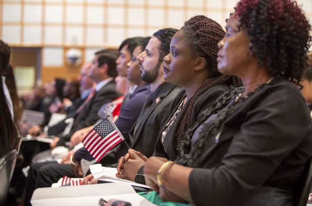 Marie Claire Kum, from Cameroon, holds a U.S. flag as she listens intently at the naturalization ceremony at the JFK Museum in Boston. (Robin Lubbock/WBUR)