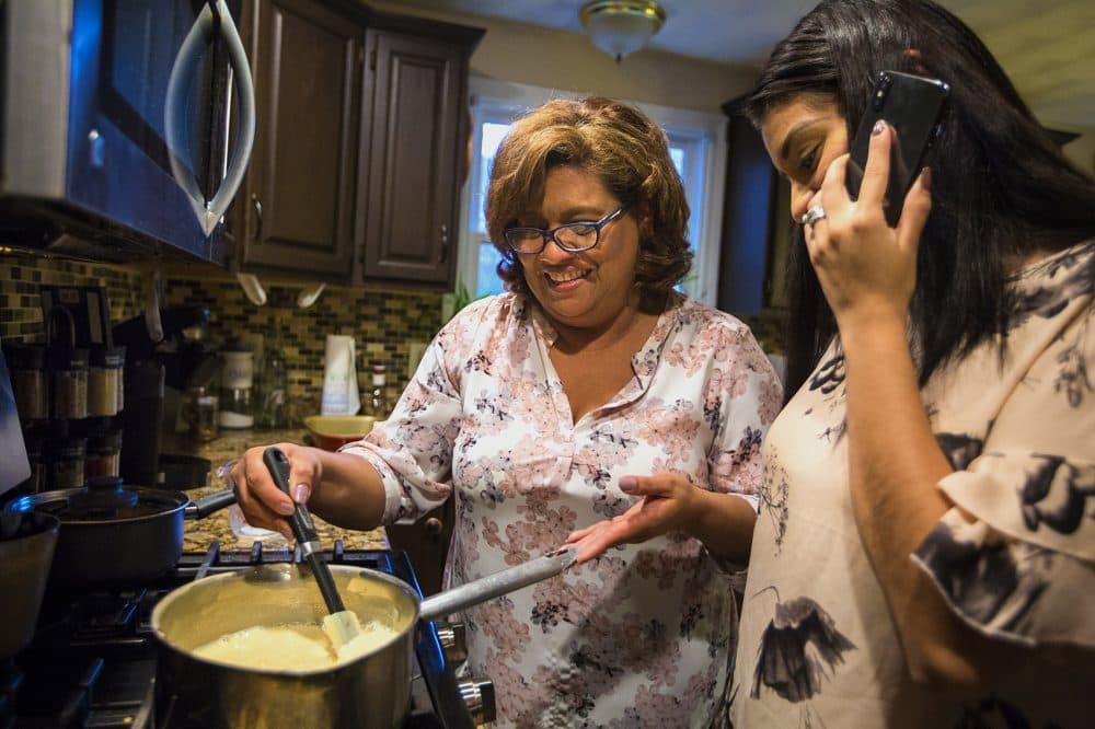 As Irma Flores stirs milk in a pan, her daughter Gabriela Portillo-Perez speaks with her grandmother Isabel on the phone in El Salvador. The Trump administration announced Monday it would be ending temporary protected status for immigrants from El Salvador. Flores and her two children are in the U.S. under the auspices of TPS. (Jesse Costa/WBUR)