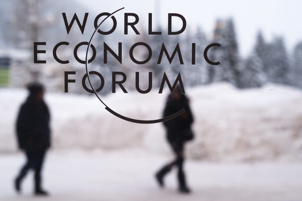 Two people walk behind the logo of the World Economic Forum at the meeting's conference center in Davos, Switzerland, Sunday, Jan. 21, 2018. The meeting brings together entrepreneurs, scientists, chief executives and political leaders from Jan. 23 to 26. (Markus Schreiber/AP)
