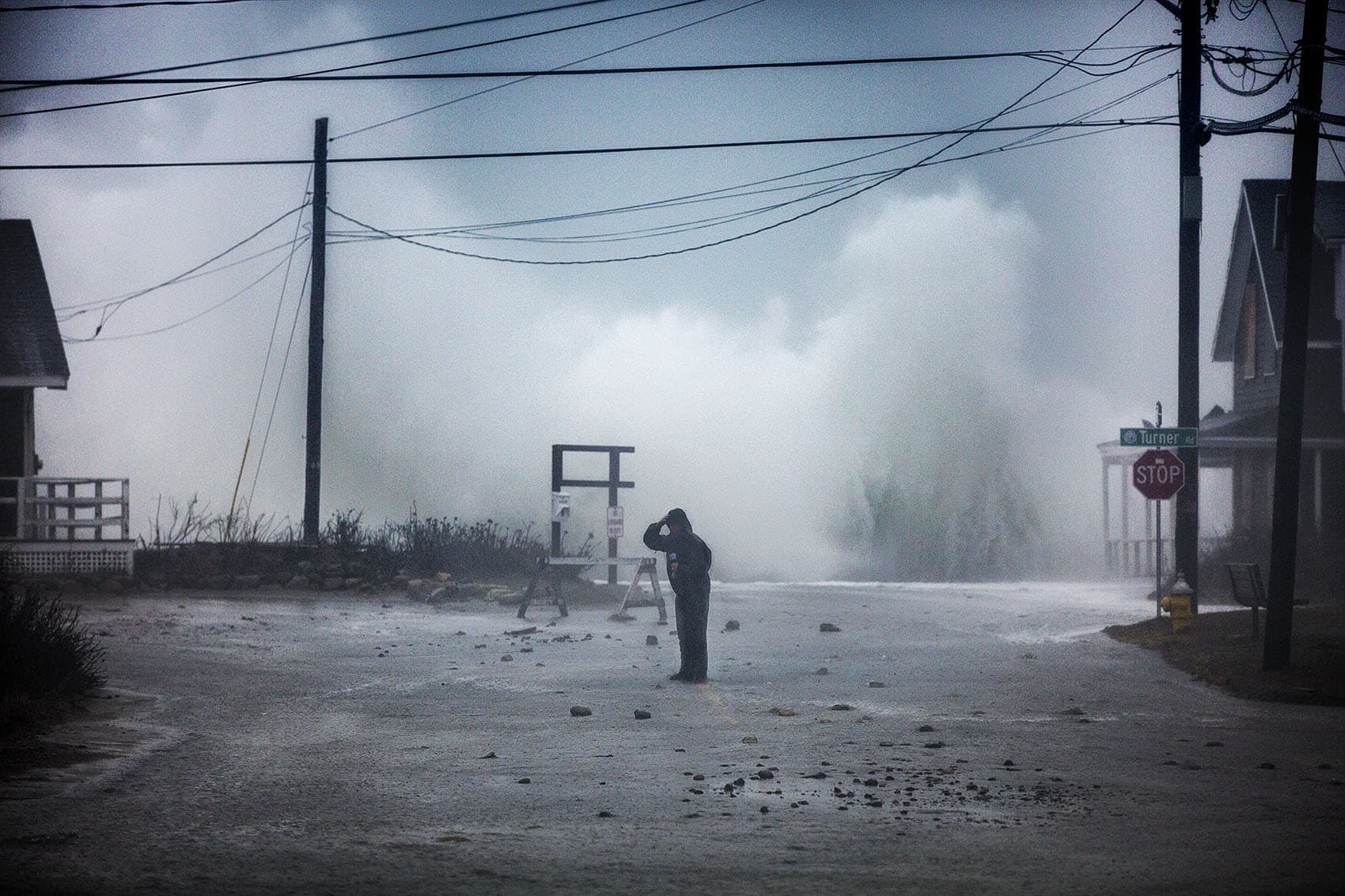 A TV news broadcaster stands in the middle of Jericho Road at Cedar Point in Scituate while waves crash on the seawall at high tide during the nor'easter on March 2. (Jesse Costa/WBUR)