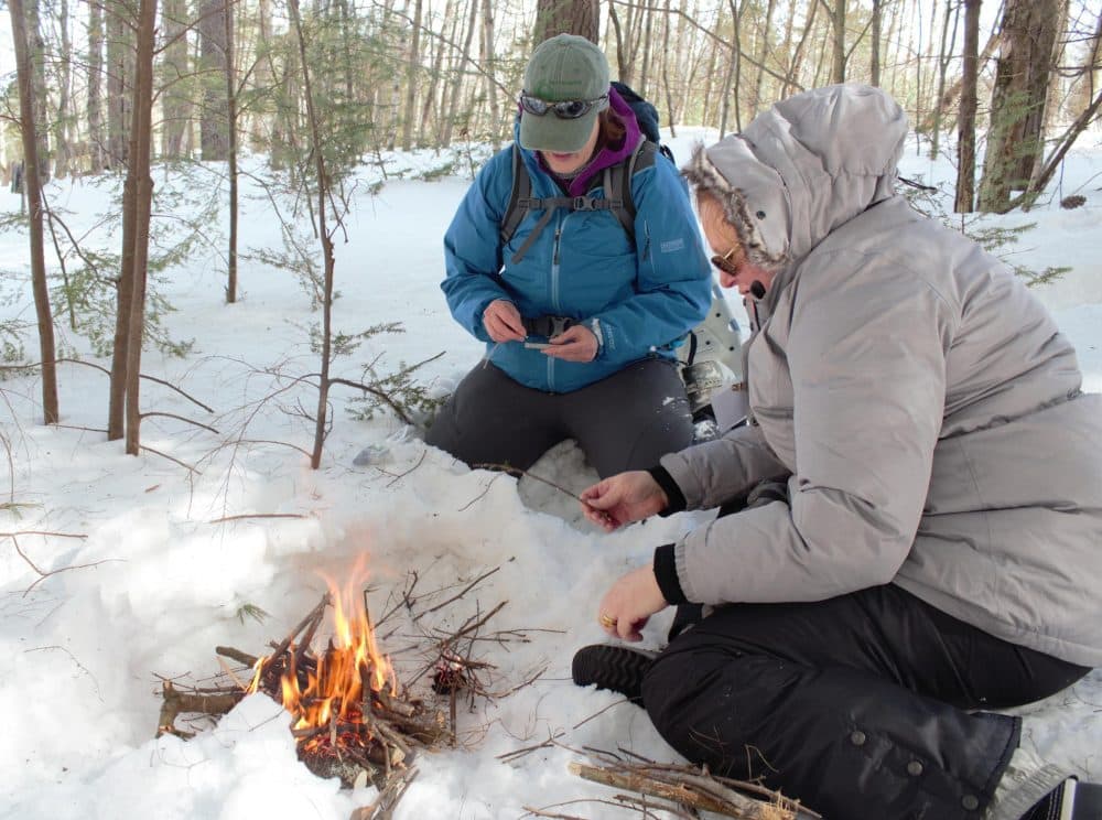 Julia Wilcox and Claire Rouge tend to a fire they made during BOW's winter survival skills class. (Annie Ropeik/NHPR)