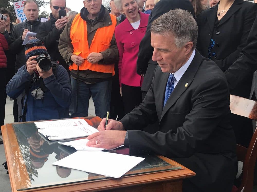 Vermont Gov. Phil Scott signs three pieces of gun control legislation amid boos and cheers on the front steps of the statehouse Wednesday. (Emily Alfin Johnson/VPR)