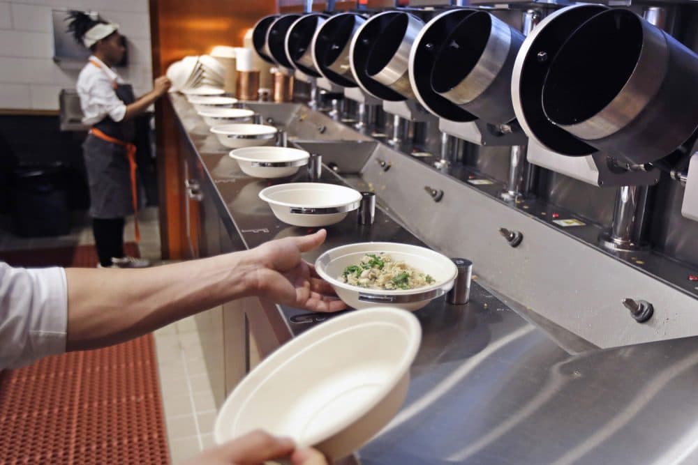 A worker lifts a lunch bowl off the production line at Spyce, a restaurant which uses a robotic cooking process, in Boston, Thursday, May 3, 2018. Robots can't yet bake a souffle or fold a burrito, but the new restaurant in Boston is employing what it calls a &quot;never-before-seen robotic kitchen&quot; to cook up ingredients and spout them into a bowl. (Charles Krupa/AP)