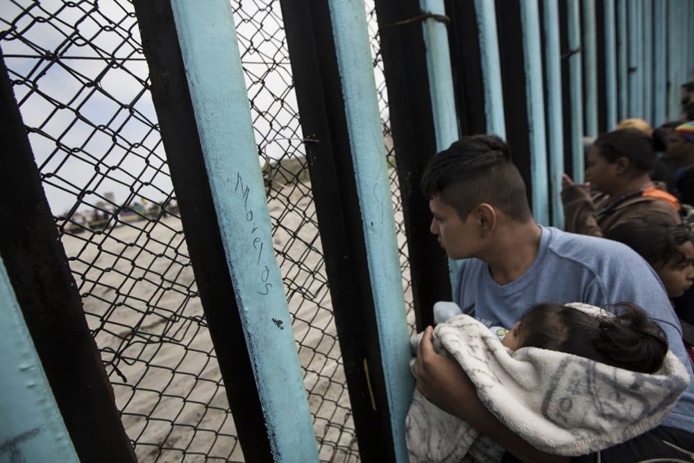 In this April 29, 2018 file photo, a member of the Central American migrant caravan, holding a child, looks through the border wall toward a group of people gathered on the U.S. side, as he stands on the beach where the border wall ends in the ocean, in Tijuana, Mexico, Sunday, April 29, 2018 (AP Photo/Hans-Maximo Musielik, File)