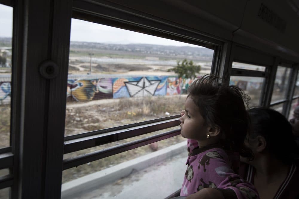 A Central American child who is traveling with a caravan of migrants, peers at the border wall from a bus carrying the group to a gathering of migrants living on both sides of the border, in Tijuana, Mexico, Sunday, April 29, 2018. U.S. immigration lawyers are telling Central Americans in a caravan of asylum-seekers that traveled through Mexico to the border with San Diego that they face possible separation from their children and detention for many months. They say they want to prepare them for the worst possible outcome. (Hans-Maximo Musielik/AP)