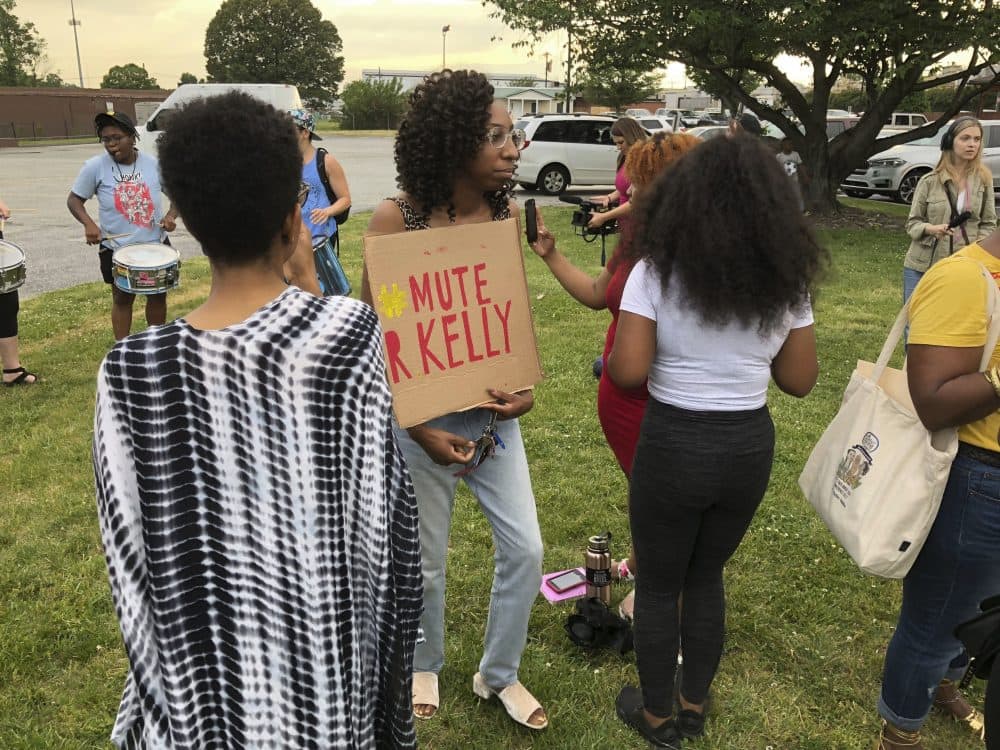 A protester carries a sign prior to a concert featuring R. Kelly in Greensboro, N.C., Friday, May 11, 2018. The group was demonstrating to protest Kelly's appearance in light of longstanding allegations of sexual misconduct and the decision by coliseum officials to proceed with the concert. Kelly denies abusing anyone and faces no current criminal charges. (AP Photo/Skip Foreman)