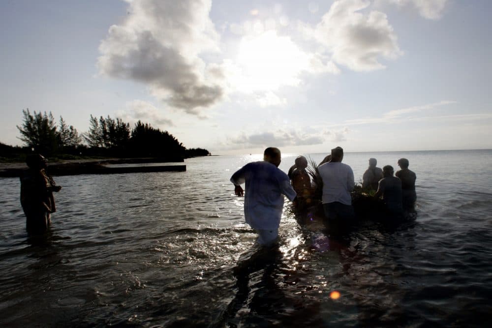 A group of men wade into the ocean as they push a small raft loaded with offerings to their ancestors out to sea Sunday, June 19, 2005 as part a Juneteenth celebration. (Wilfredo Lee/AP)