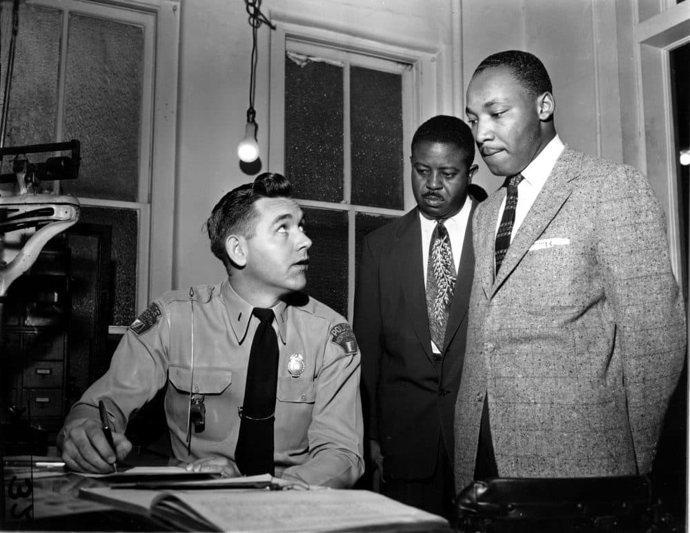 The Rev. Martin Luther King Jr., right, accompanied by Rev. Ralph D. Abernathy, center, is booked by city police Lt. D.H. Lackey in Montgomery, Ala., on Feb. 23, 1956. (Gene Herrick/AP)