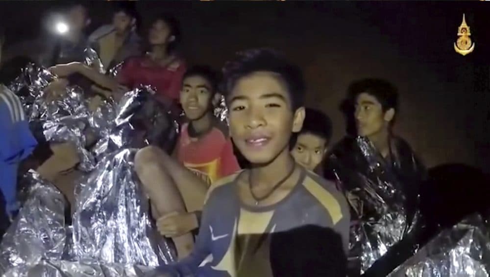 In this July 3, 2018, image taken from video provided by the Royal Thai Navy Facebook Page, Thai boys smile as Thai Navy SEAL medic help injured children inside a cave in Mae Sai, northern Thailand. The Thai soccer teammates stranded more than a week in the partly flooded cave said they were healthy on a video released Wednesday, as heavy rains forecast for later this week could complicate plans to safely extract them. (Royal Thai Navy Facebook Page via AP)
