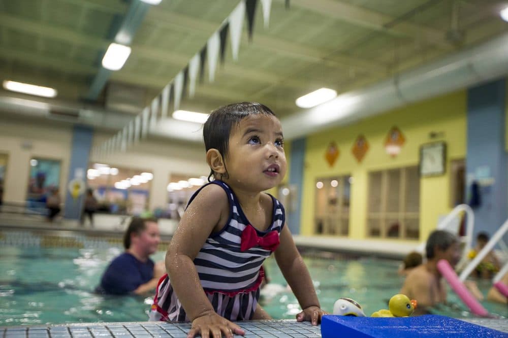 In addition to getting used to being in water and swimming, children also learn how to enter and exit the pool properly. Twenty-two-month-old Charlotte Joshi climbs out of the pool during a toddler swim class at the YMCA in Waltham. (Jesse Costa/WBUR)