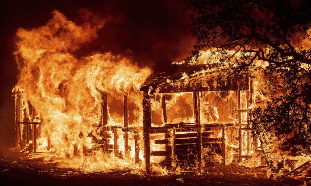 In this Thursday, July 26, 2018 file photo, a structure burns as the Carr fire races along Highway 299 near Redding, Calif. In the last year, fires have devastated neighborhoods in the Northern California wine country city of Santa Rosa, the Southern California beach city of Ventura and, now, the inland city of Redding. Hotter weather from changing climates is drying out vegetation, creating more intense fires that spread quickly from rural areas to city subdivisions, climate and fire experts say. But they also blame cities for expanding into previously undeveloped areas susceptible to fire. (Noah Berger/AP)