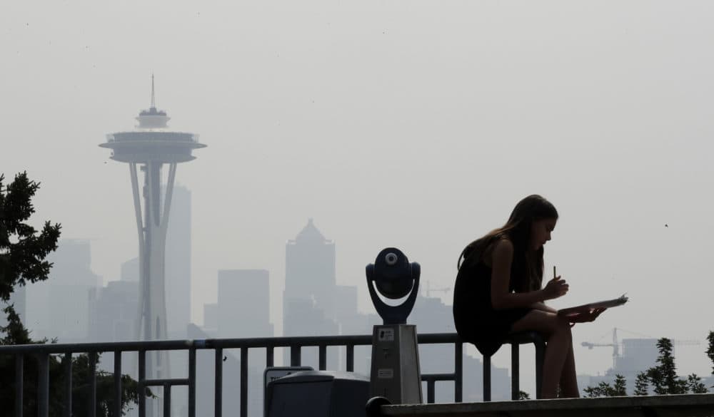 A girl works on a drawing next to an unused viewing scope as a smoky haze obscures the Space Needle and downtown Seattle behind, Tuesday, Aug. 14, 2018. Public-health officials are warning of unhealthy air across parts of the Pacific Northwest as smoke from wildfires move across the region. (Elaine Thompson/AP)