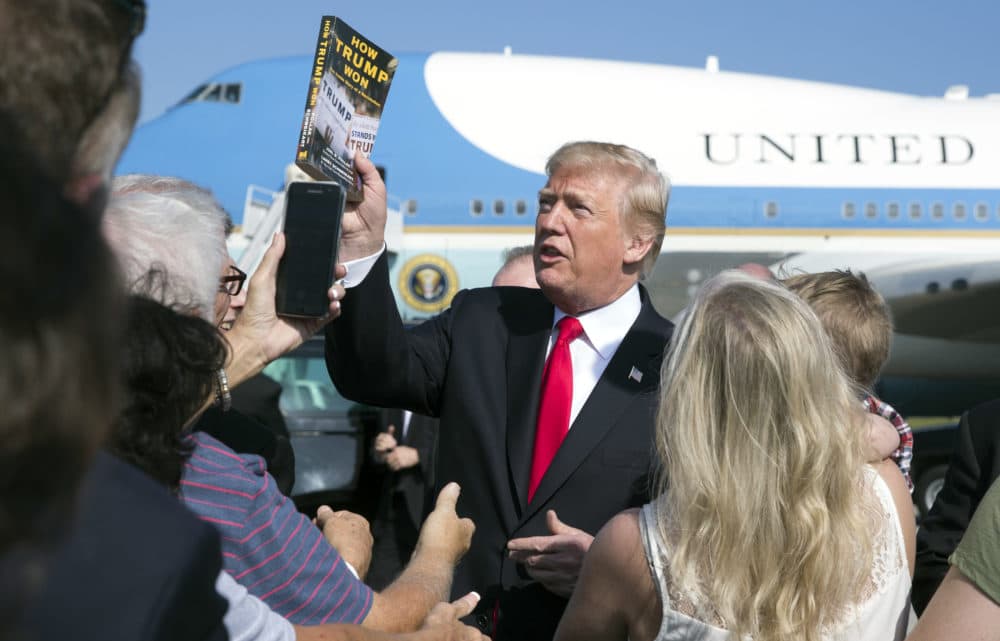 President Donald Trump holds up the book &quot;How Trump Won The Inside Story of a Revolution&quot; as he greets people on the tarmac as he arrives on Air Force One at Palm Beach International Airport, in West Palm Beach, Fla., Friday, Dec. 22, 2017. (Carolyn Kaster/AP)