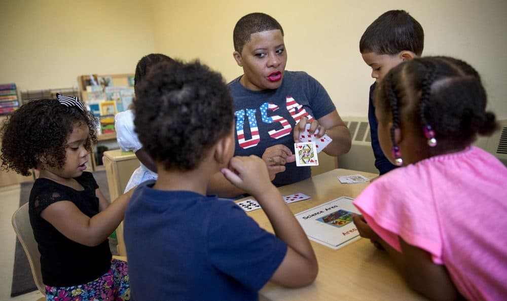 Teacher Nicole Parker-Mondon sits at a table with students, using playing cards as a teaching aid. (Robin Lubbock/WBUR)