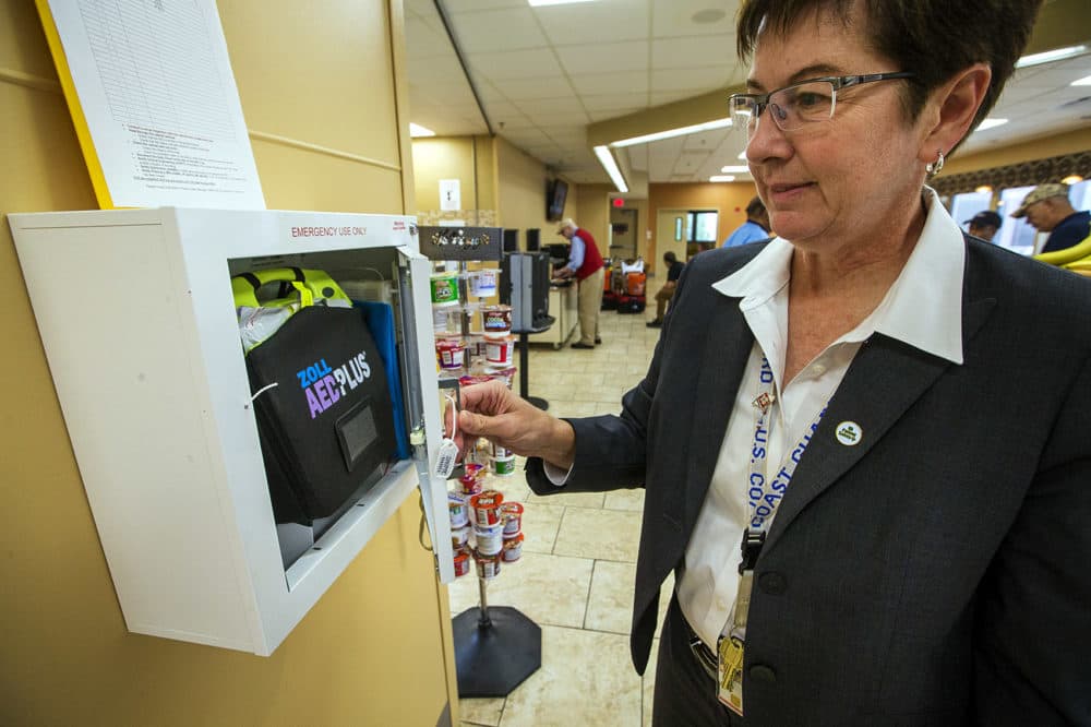Pam Bellino, patient safety manager for VA Boston, opens an AED box located in the cafeteria at the West Roxbury VA Medical Center, with the naloxone kit, the blue pouch, tucked on the side next to the defibrillator. (Jesse Costa/WBUR)