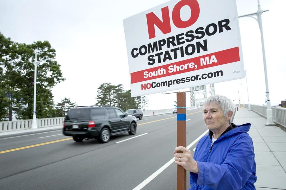 Mernie Clifton demonstrates against the proposed gas compressor, as cars drive by on the Fore River Bridge in Weymouth. (Robin Lubbock/WBUR)