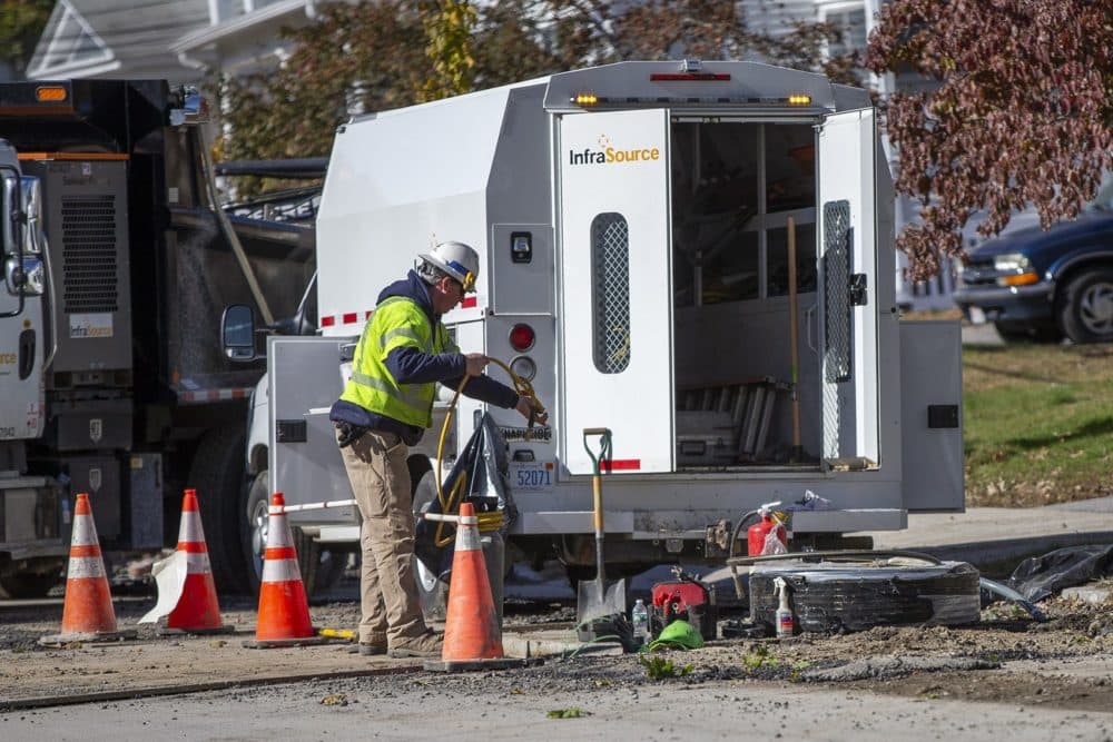 In late October, a utility worker hands a hose to another worker repairing gas lines underground on Salem Street in Lawrence. (Jesse Costa/WBUR)