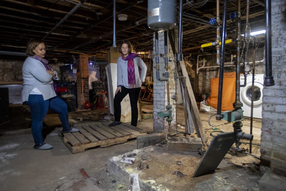 Sadia Jiminian, left, shows where the furnace was in the basement of her Lawrence home before it caught on fire during the gas explosion on Sept. 13. (Jesse Costa/WBUR)