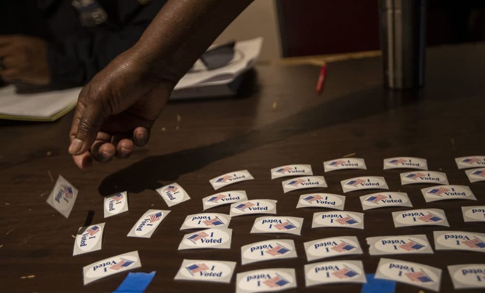 An election worker at Morning Star Baptist Church lays down “I Voted” stickers on a table for voters to pick up after they have voted. (Jesse Costa/WBUR)