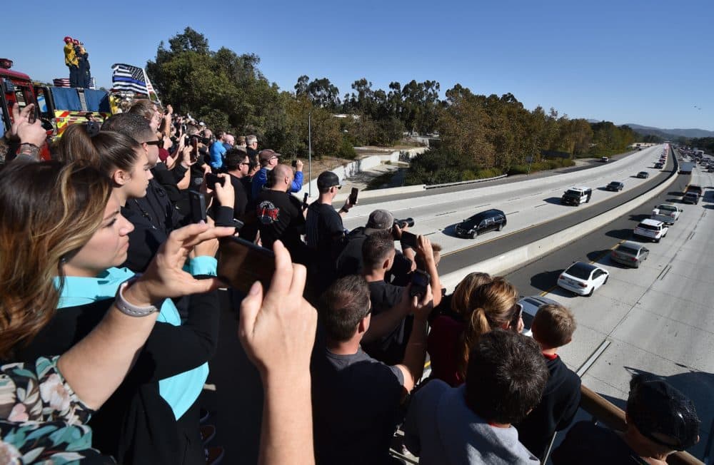 Firefighters, law enforcement and members of the public watch as the hearse carrying the body of Ventura County Sheriff's Sgt. Ron Helus, the first victim named in the mass shooting at a country bar in Thousand Oaks, Calif., is transported in a procession Nov. 8, 2018. (Robyn Beck/AFP/Getty Images)