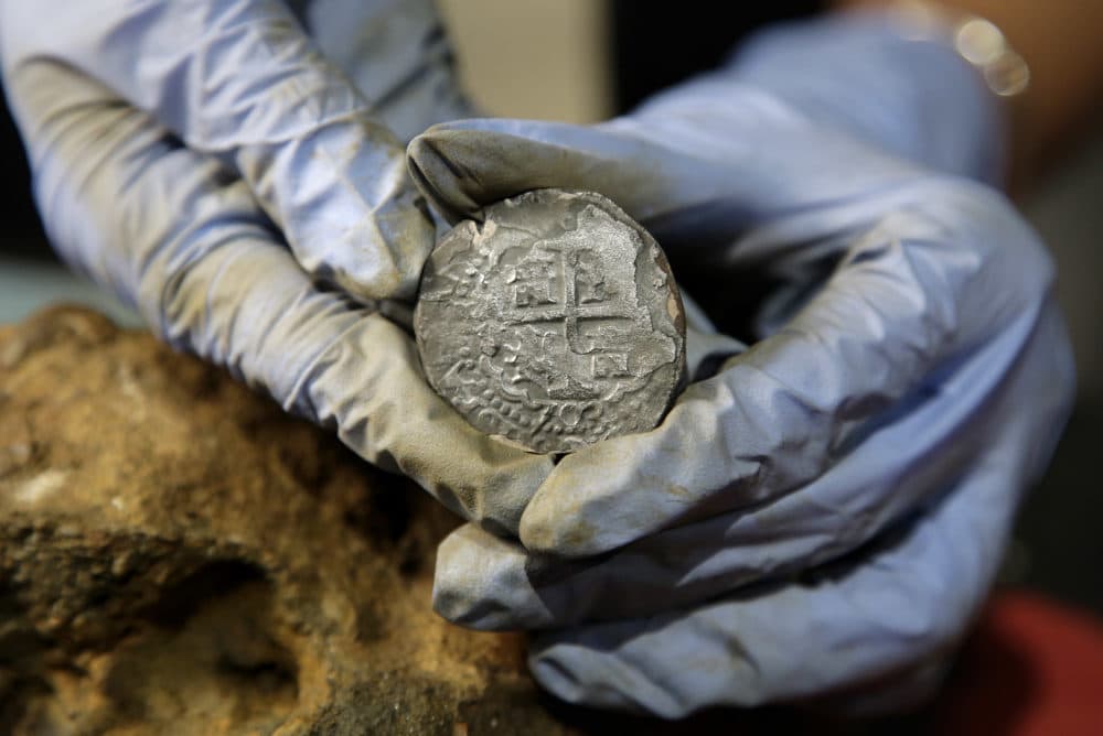 In this Wednesday, Sept. 21, 2016 photo, archaeologist Marie Kesten Zahn, of Yarmouth, Mass. displays a silver coin recovered from the wreckage of the pirate ship Whydah Gally at the Whydah Pirate Museum, in Yarmouth. The undersea explorer Barry Clifford, who discovered the Whydah Gally, the first authenticated pirate shipwreck in U.S. waters, says he’s finally found where the ship’s vaunted treasure lies after more than 30 years of poking around the murky waters off Cape Cod. (AP Photo/Steven Senne)