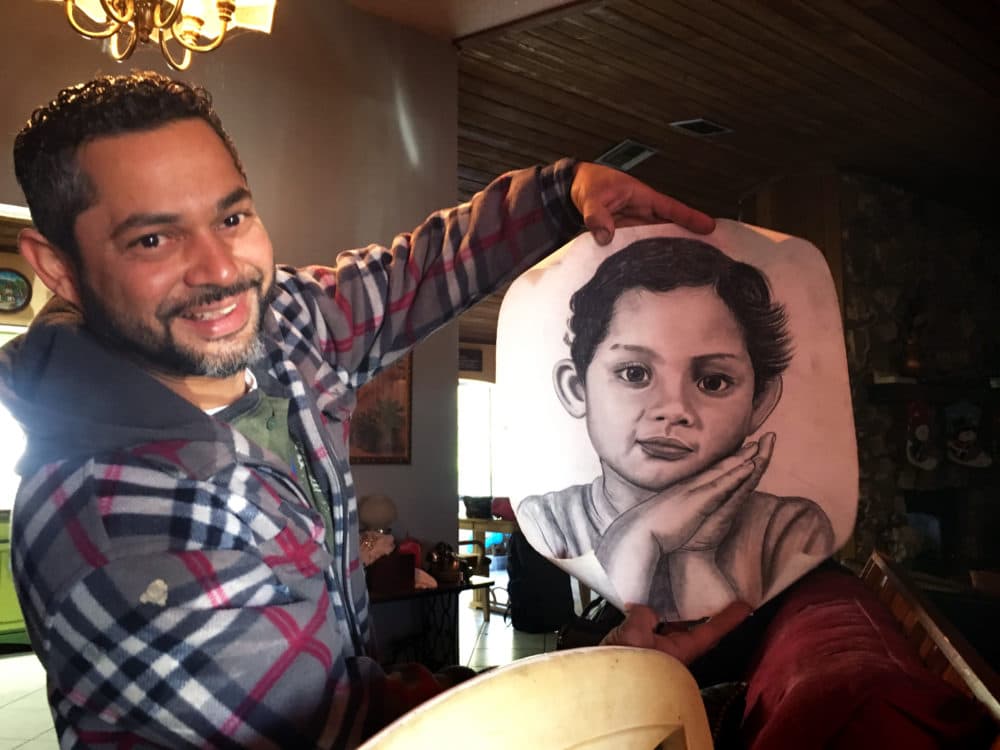 Roque Cartagena holds up a charcoal portrait he made of his daughter when she was a baby. (Kelly Horan/WBUR)