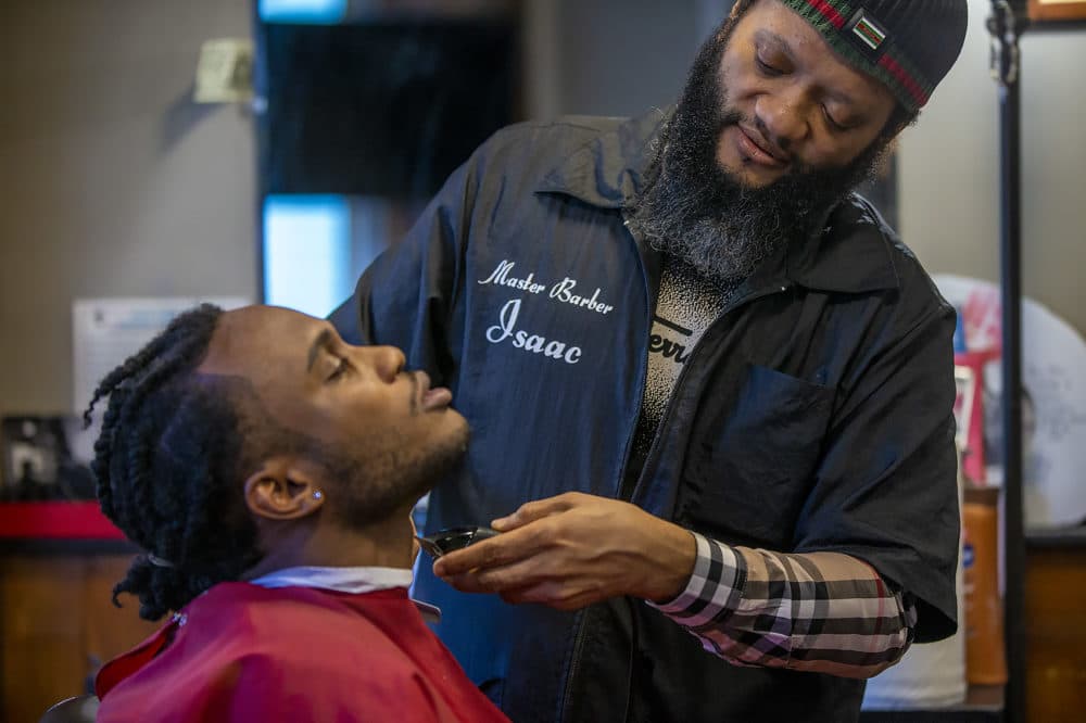 Master barber Isaac Genty trims the beard of his son Bright, who is training to become a barber himself at Headlines Unisex Barber Shop in Cambridge. (Jesse Costa/WBUR)