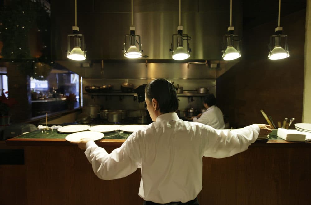 A waiter reaches for plates at a restaurant in San Francisco. Nearly all restaurants in the U.S. operate under the tip system: Servers and those in the back of the house — chefs, line cooks, dishwashers, etc. — are paid a lower-than-average standard minimum wage, and then they earn tips to make up for the pay disparity. (Eric Risberg/AP)