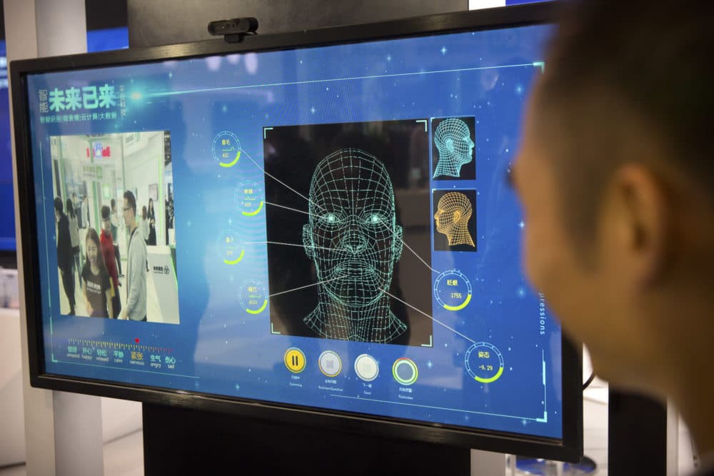 A man watches as a visitor tries out a facial recognition display at a booth for Chinese tech firm Ping'an Technology at the Global Mobile Internet Conference (GMIC) in Beijing on April 26, 2018. (Mark Schiefelbein/AP)