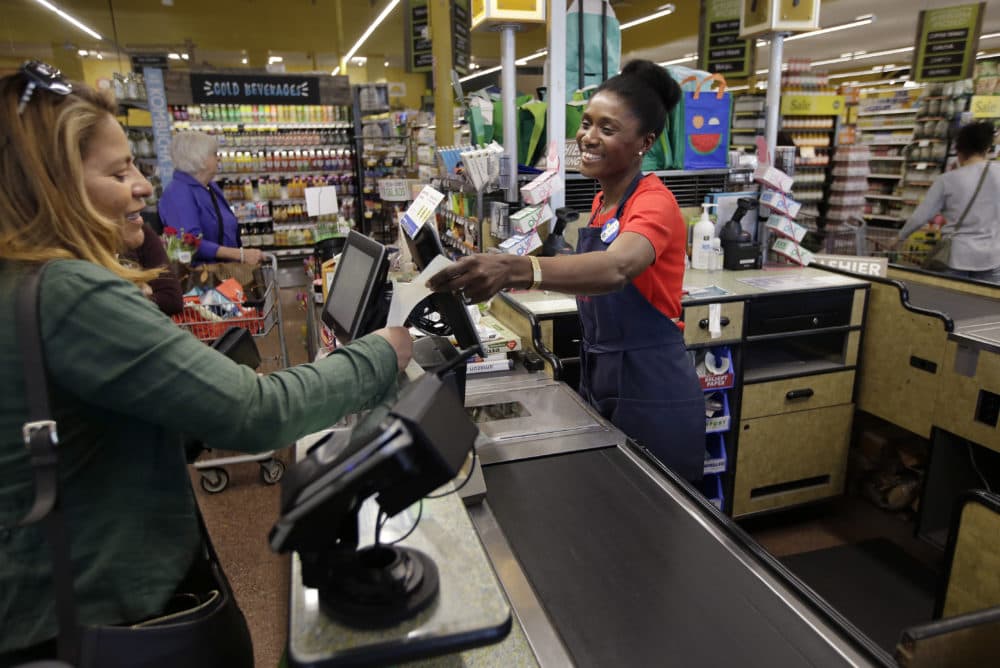 Retail workers are among those that will see their base wages increase under the new law. In this May 2018 photo, Nadine Vixama works as a cashier at a Whole Foods in Cambridge, Mass. (AP Photo/Steven Senne)