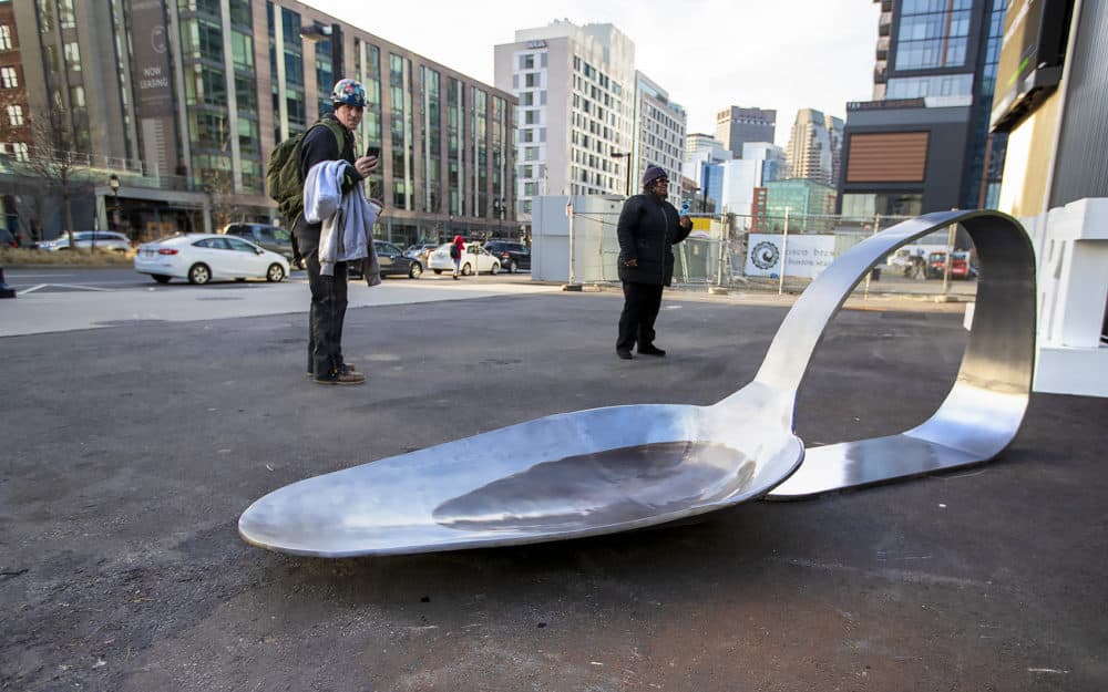 Patrick Lynch, left, a metal fabricator working on one of the buildings being erected in the Seaport, takes a photo of the 800-pound, 11-foot-long steel spoon as he passes by District Hall on his way home. He says he is currenlty in recovery for opioid addiction and thinks it's great the conference is happening and people are talking about the issue. (Jesse Costa/WBUR)