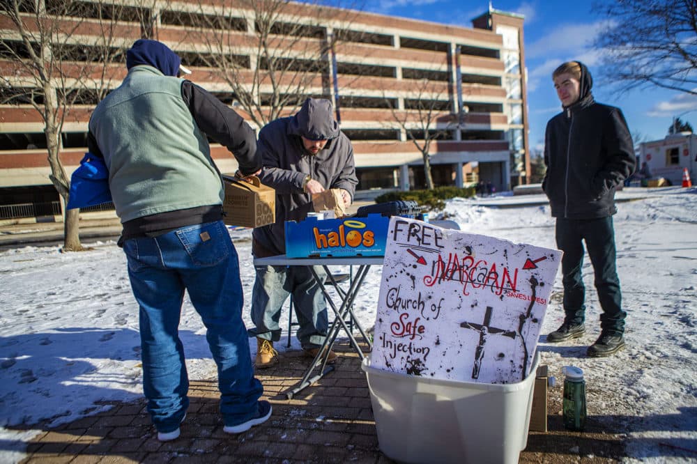 On a frigid 17º F afternoon in Pickering Square in Bangor, Maine, two men stop by a folding table set up by The Church of Safe Injection for some coffee. (Jesse Costa/WBUR)