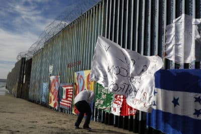 Joseph, an migrant from Honduras, plants a white flag with the words, &quot;peace and God with us,&quot; in front of the border wall during an art display on the border wall, topped with razor wire, Tuesday, Jan. 8, 2019, on the beach in Tijuana, Mexico. (Gregory Bull/AP)