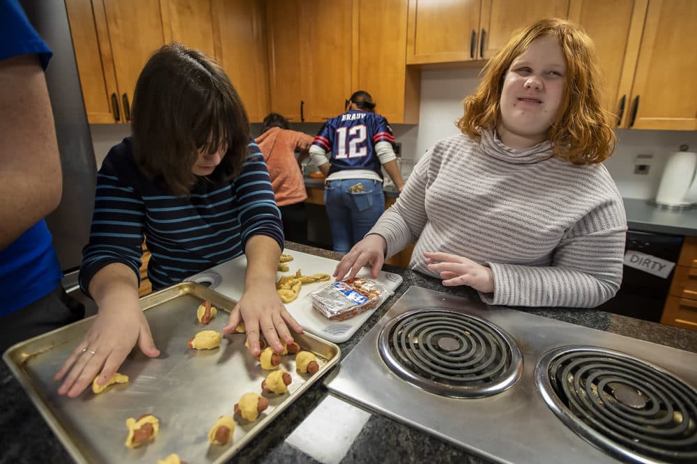 Haley Valente, left, and Sophie Brown wrap miniature hot dogs with crescent dough to make pigs in a blanket for their Super Bowl watch party organized by the students of the College Success program at the Perkins School for the Blind. (Jesse Costa/WBUR)