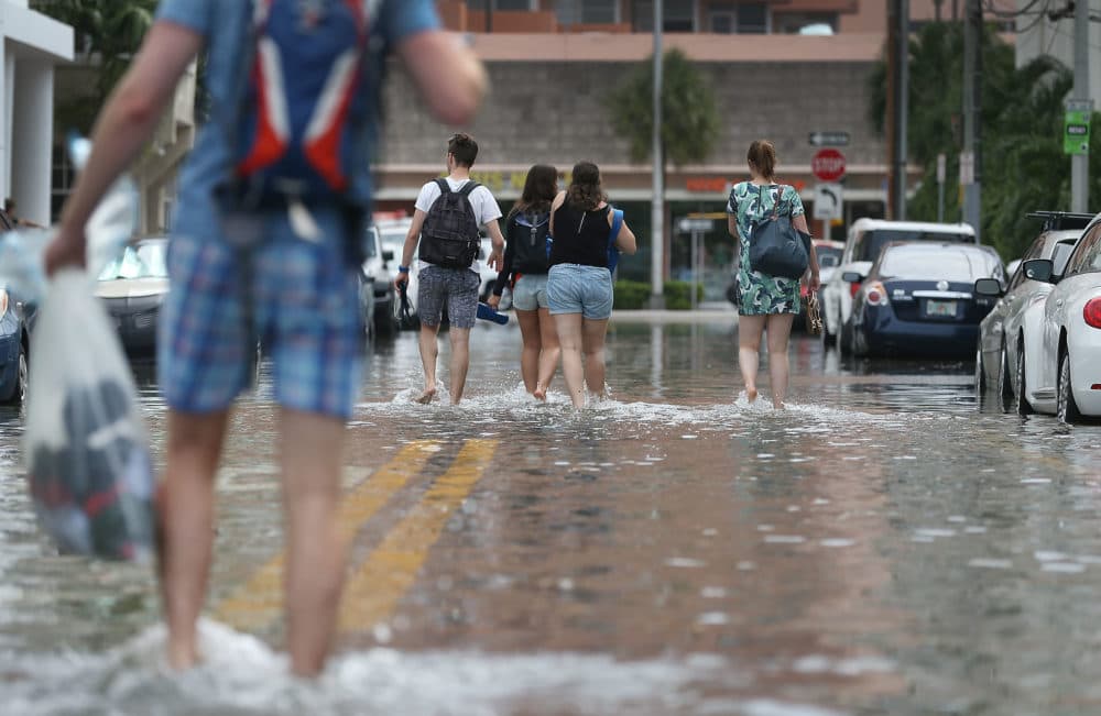 People walk through a flooded street that was caused by the combination of the lunar orbit which caused seasonal high tides, and what many believe is the rising sea levels due to climate change, in Miami Beach, Fla. (Joe Raedle/Getty Images)