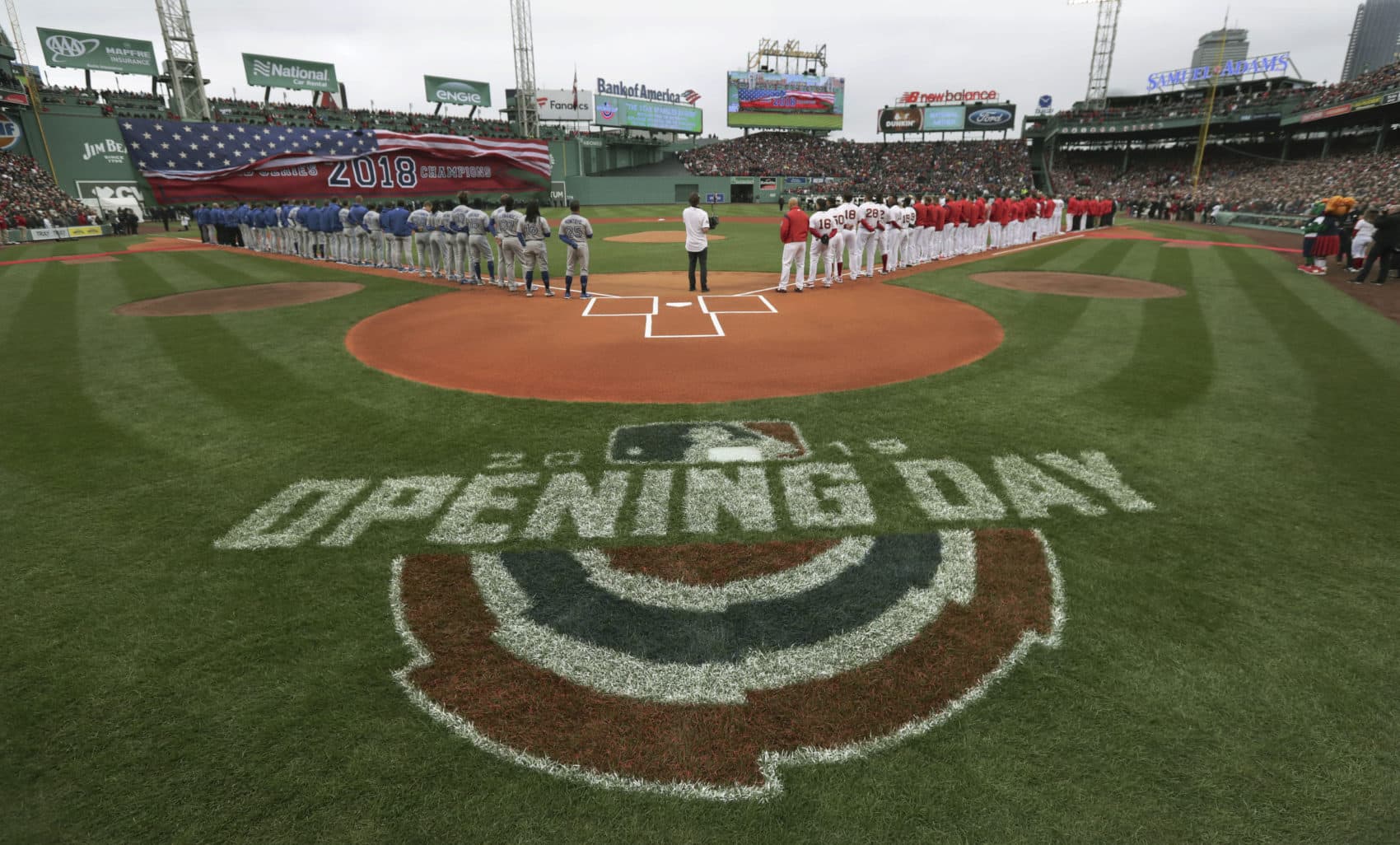 The Toronto Blue Jays, left, and Boston Red Sox stand along the base lines during the national anthem before the home opener baseball game on Tuesday in Boston. (Charles Krupa/AP)