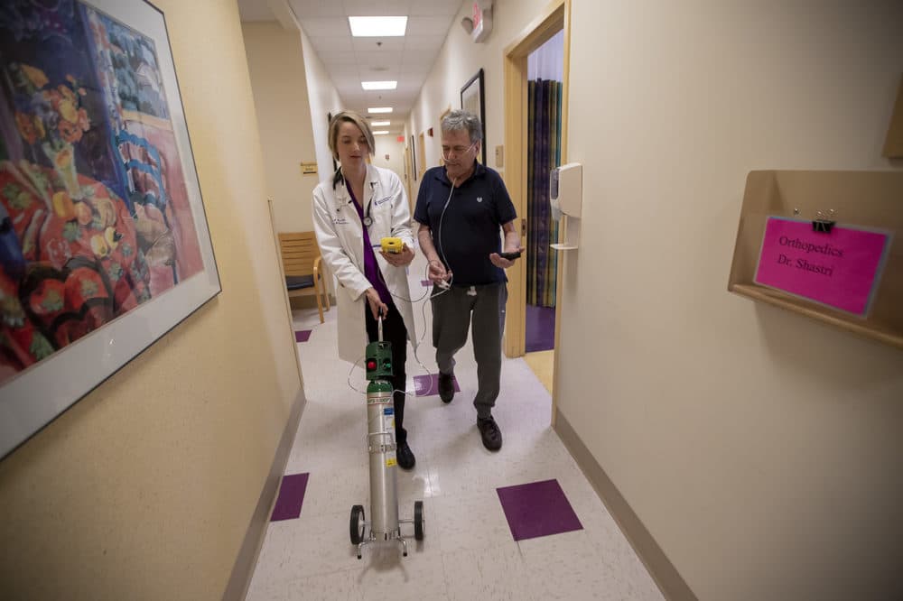 Dr. Mary Rice walks with Michael Howard, who has the progressive lung disease COPD, as they test oxygen levels with a portable tank. (Jesse Costa/WBUR)