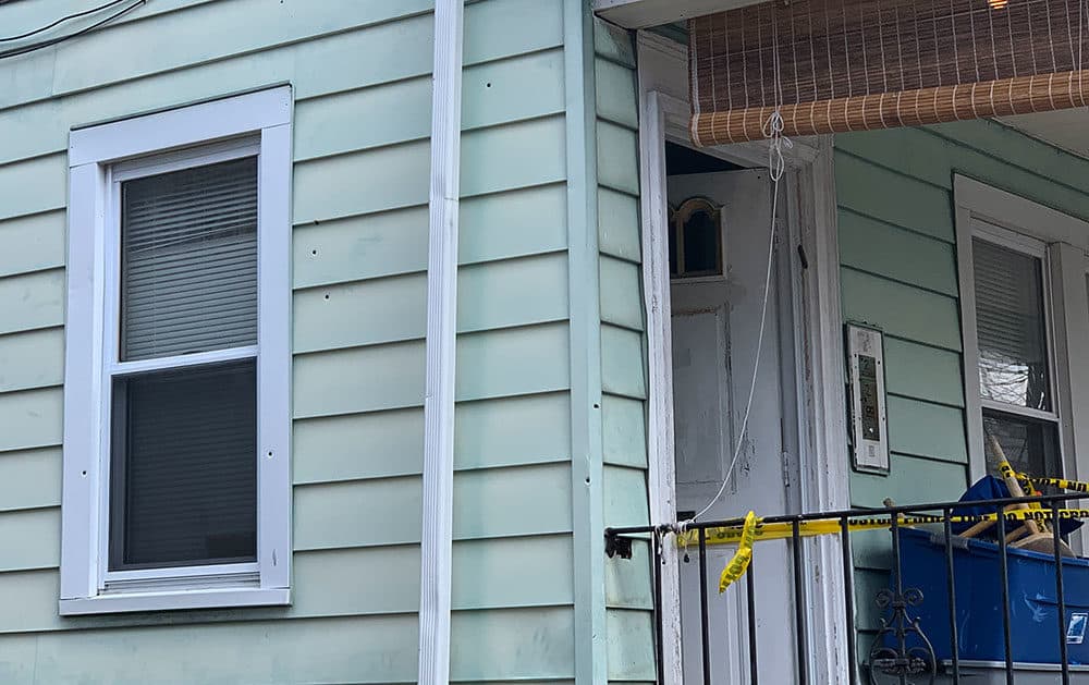 Bullet holes and police tape are seen on the side of the Mattapan home. (Simon Rios/WBUR)